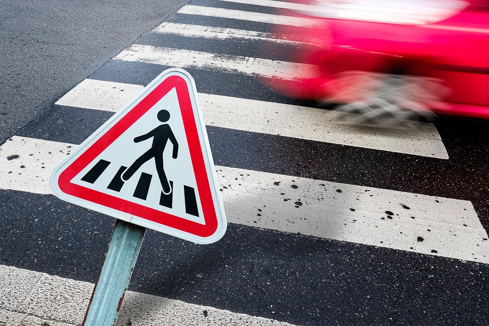 pedestrian crossing sign in front of a pedestrian crossing with red car speeding by