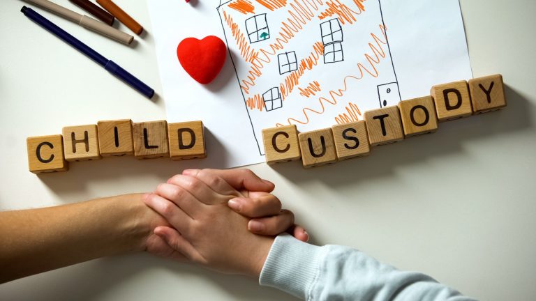 child custody spelled out with blocks as a parent and child hold hands