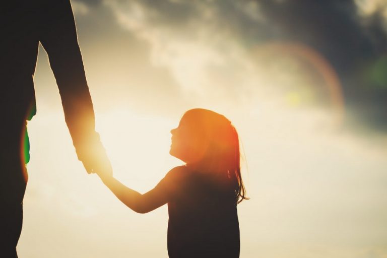 A young child holding hand with a parent as the sun is about to set